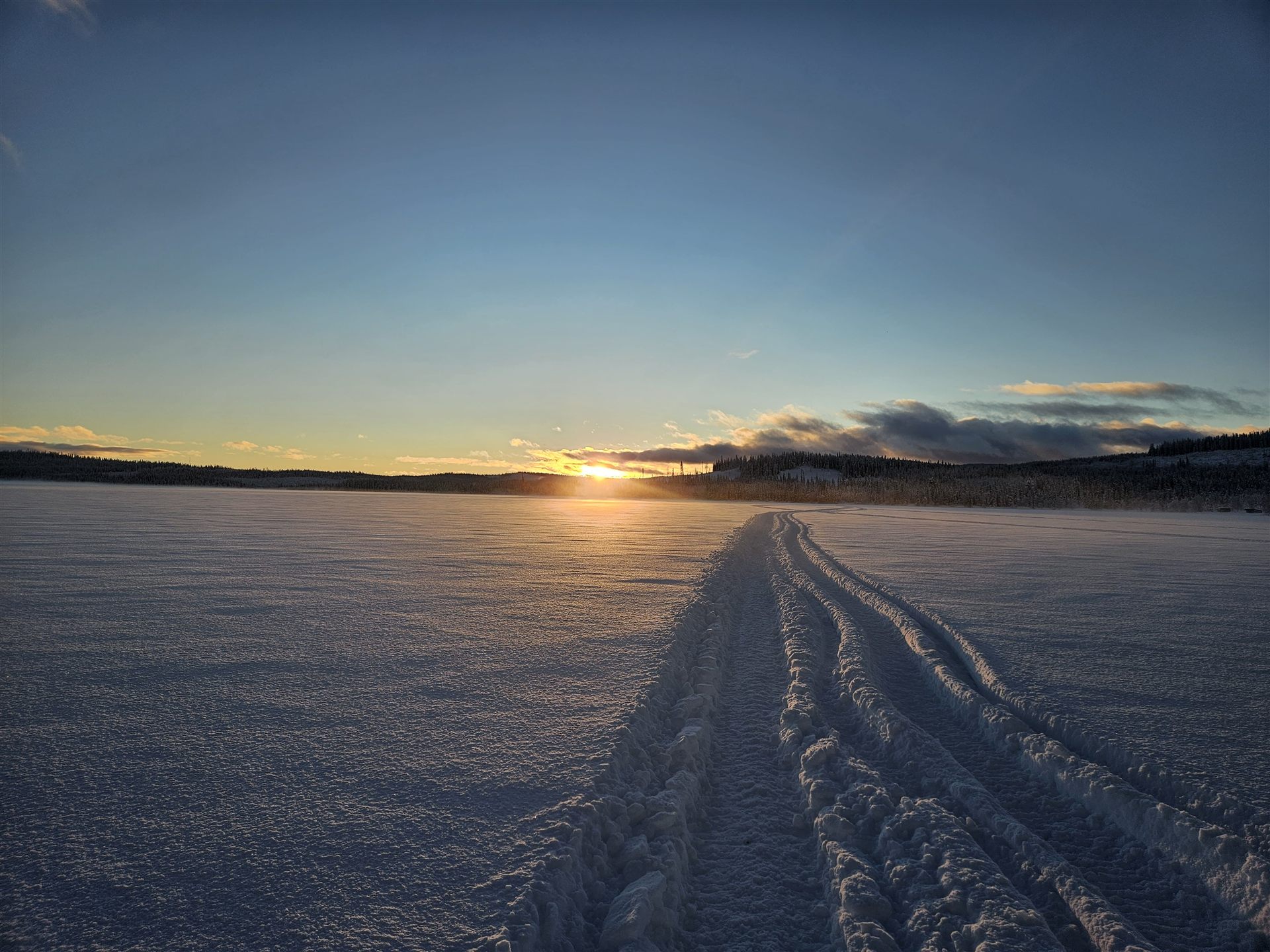Sonnenuntergang ueber einer Schneespur auf weiter Flaeche